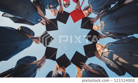 Group of students wearing graduation gowns making circle with their graduation caps against blue sky. 121524008
