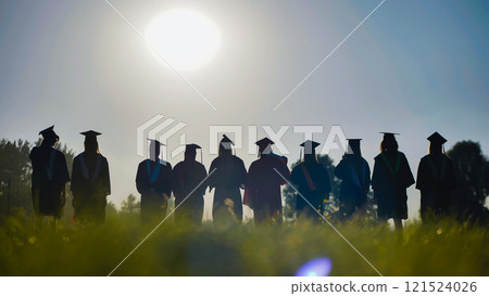 Graduates in cap and gown stand in a field at sunset, commemorating their high school graduation 121524026
