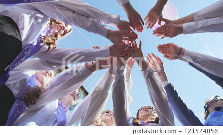Students celebrating last day of school, wearing sashes and white shirts, arms raised in unity under blue sky. Joyful achievement and hope for future 121524056