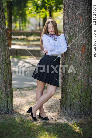 Confident student leaning against tree in a park, wearing school uniform on her first day Confident student leaning against tree in a park, wearing school uniform on her first day 121524073