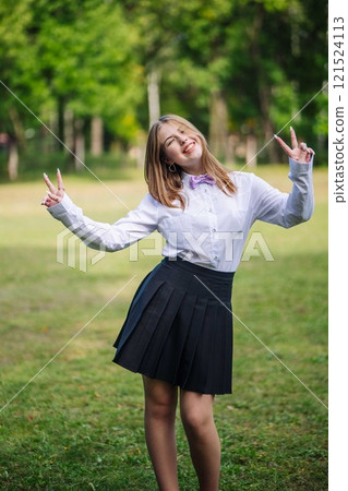 Girl in school uniform with bow tie making peace sign, winking and smiling on her first day of school Girl in school uniform with bow tie making peace sign, winking and smiling on her first day of school 121524113