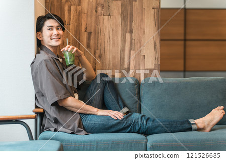 A man drinks green smoothies, green juices, and vegetable juices on his sofa at home to fast, fast, and diet. A man drinks green smoothies, green juices, and vegetable juices on his sofa at home to fast, fast, and diet. 121526685