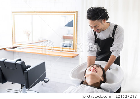 A male hairdresser washing his hair at the shampooing station in a beauty salon and a Japanese female customer having her hair washed; the woman has no face A male hairdresser washing his hair at the shampooing station in a beauty salon and a Japanese female customer having her hair washed; the woman has no face 121527288