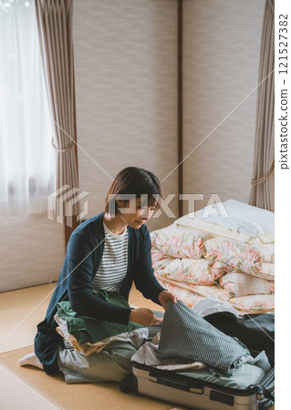 A woman putting clothes into a suitcase and getting ready to go home at an inn 121527382