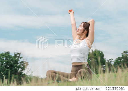 A woman taking a deep breath, refreshing, doing yoga, stretching, and pilates in the grassland (healthcare and diet) 121530061
