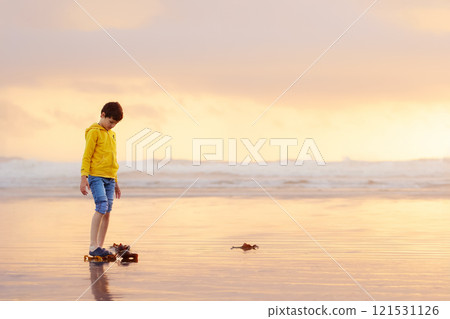 Boy is walking in the ocean beach in orange sunset time. Boy is walking in the ocean beach in orange sunset time. 121531126