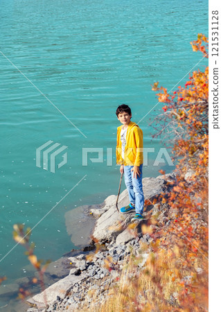 Teenage boy is enjoying a sunny fall day and the turquoise waters of the mountain river on his hike. Yellow foliage. 121531128