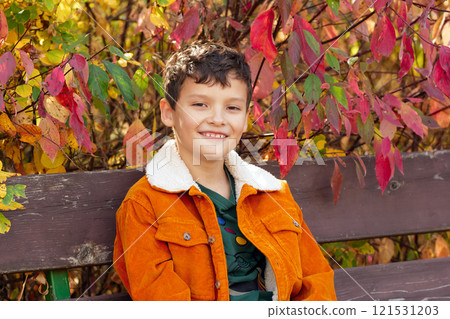 Boy in orange jacket sitting on the bench in autumn park. Boy in orange jacket sitting on the bench in autumn park. 121531203
