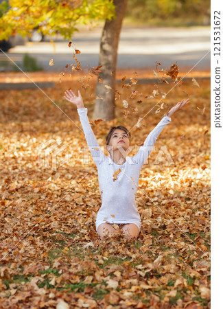 Girl is sitting on the ground in the fall park and throwing yellow leaves. Girl is sitting on the ground in the fall park and throwing yellow leaves. 121531672