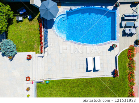 Aerial view of a stylish backyard pool with curved design, surrounding green lawn, and cozy patio seating 121531958