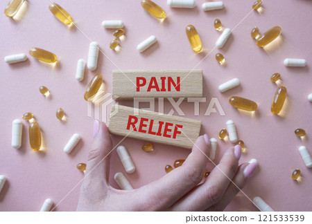 Pain Relief symbol. Concept word Pain Relief on wooden blocks. Beautiful pink background with pills. Doctor Hand. Medicine and Pain Relief concept. Copy space 121533539