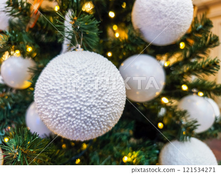 Decorated Christmas tree with white ornaments and glowing lights in festive setting 121534271