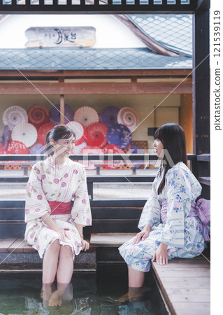 Two young women in yukata soaking their feet in a footbath [Filming cooperation: Shibata City Film Commission Council] 121539119
