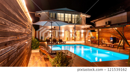 Modern swimming pool with outdoor shower and wooden loungers at night. Concept of luxurious backyard escape Modern swimming pool with outdoor shower and wooden loungers at night. Concept of luxurious backyard escape 121539162