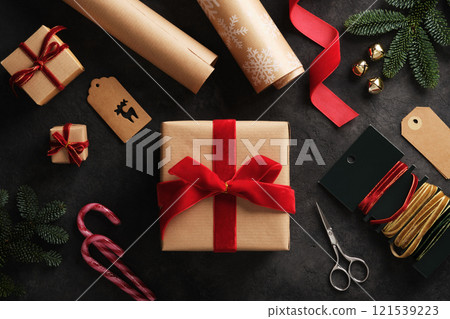 Holiday preparation, wrapped gift in a kraft brown box with red velvet ribbon and gift wrapping supplies all around 121539223
