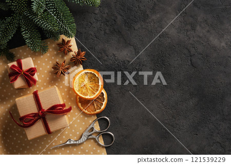 Banner with wrapping supplies for Christmas and new year gifts. Kraft paper, scissors, dried orange, anise stars, spruce branch on dark background. Place for your text. Banner with wrapping supplies for Christmas and new year gifts. Kraft paper, scissors, dried orange, anise stars, spruce branch on dark background. Place for your text. 121539229