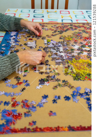 Female hands collect scattered puzzles on a brown background. Board games, hobby, leisure. Entertainment concept 121539288
