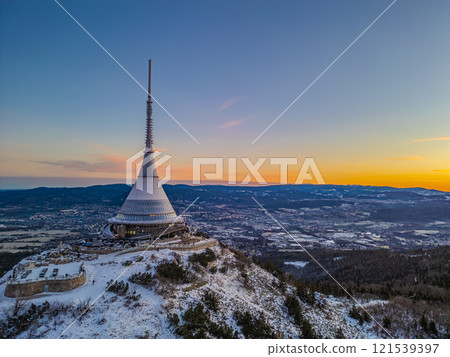 Snow blankets Jested Mountain as dawn breaks, casting a warm glow across the landscape. The iconic tower stands tall against the vibrant colors of the sky, creating a serene winter vista. Snow blankets Jested Mountain as dawn breaks, casting a warm glow across the landscape. The iconic tower stands tall against the vibrant colors of the sky, creating a serene winter vista. 121539397