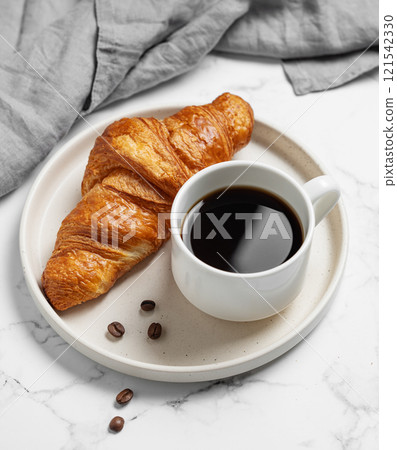 Cup of  espresso coffee and fresh croissant on white plate on marble background with napkin. 121542330