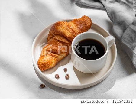 Cup of espresso coffee and fresh croissant on white plate on light textured background with shadow Cup of espresso coffee and fresh croissant on white plate on light textured background with shadow 121542332