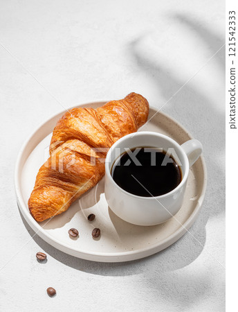 Cup of freshly brewed espresso coffee and fresh croissant on white plate on light background Cup of freshly brewed espresso coffee and fresh croissant on white plate on light background 121542333