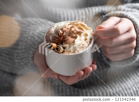 Cup of hot chocolate with whipped cream, cinnamon and anise in hands against the background  121542346