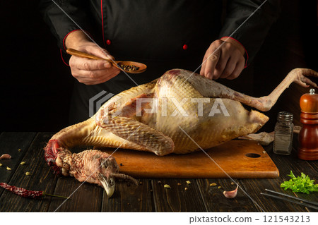 A chef seasons a fresh turkey with dry pepper in a cozy kitchen setting. The concept of preparing a national dish from a large bird for dinner. American cuisine A chef seasons a fresh turkey with dry pepper in a cozy kitchen setting. The concept of preparing a national dish from a large bird for dinner. American cuisine 121543213