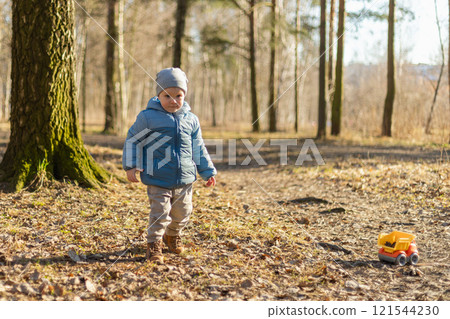 Happy baby child outdoor. Little toddler boy with toy car having fun on walk in park. Baby son smiling playing outdoor. Little child resting walking in nature. Little toddler child having fun on walk 121544230