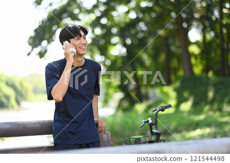Young adult man having a phone conversation while standing next to a bicycle Young adult man having a phone conversation while standing next to a bicycle 121544498