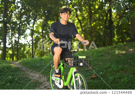 Handsome asian man riding bike through a serene park on sunny day. 121544499