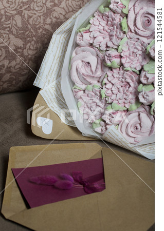 A bouquet of marshmallows. Zephyr flowers. Packed in craft paper. Next to it is a greeting card in an envelope. Close-up. 121544581