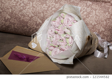 A bouquet of marshmallows. Zephyr flowers. Packed in craft paper. Next to it is a greeting card in an envelope. Close-up. A bouquet of marshmallows. Zephyr flowers. Packed in craft paper. Next to it is a greeting card in an envelope. Close-up. 121544582