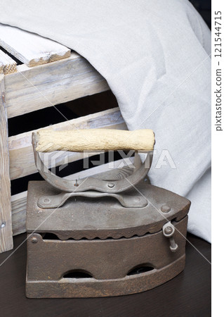 Old iron, heated by hot coals. Standing next to a wooden box and linen cloth. Old iron, heated by hot coals. Standing next to a wooden box and linen cloth. 121544715