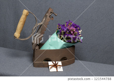 Old iron, heated by hot coals. A bouquet of dried flowers is embedded in the slightly open iron. Nearby is a greeting card. 121544788