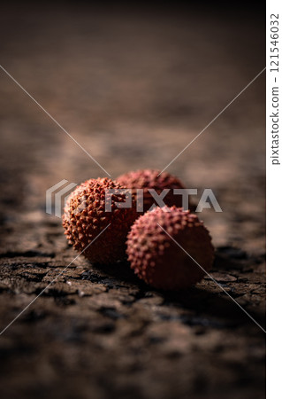 Three lychees sit on cracked dark surface 121546032