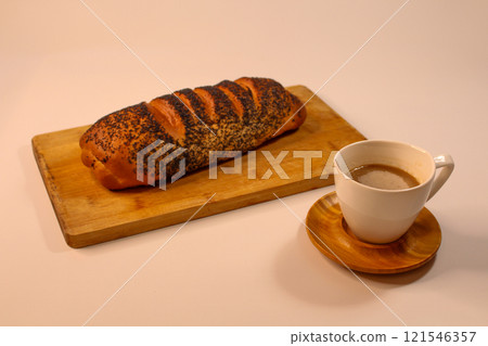 Poppy seed bun lying on a wooden board with a hot cup of coffee. Poppy seed bun lying on a wooden board with a hot cup of coffee. 121546357