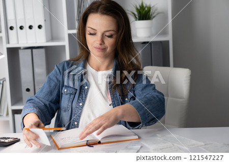 A focused woman organizing her notes in a modern, spacious office designed for productivity and inspiration, highlighting her business lifestyle and creative administration skills 121547227