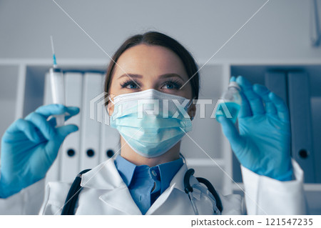 A dedicated medical professional carefully preparing an injection using a vaccine vial in a clinical setting, ensuring all safety and sterile protocols are strictly followed to protect patient health 121547235
