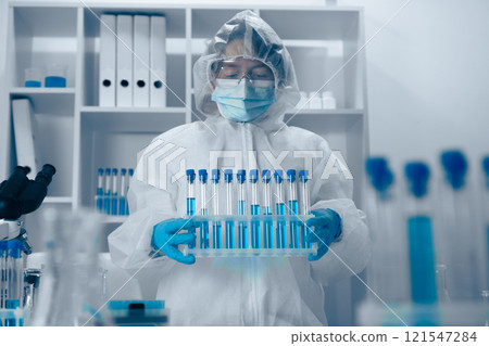 A diligent laboratory researcher is expertly handling test tubes while dressed in full protective gear, ensuring safety and accuracy in their vital work involving complex experiments and analysis A diligent laboratory researcher is expertly handling test tubes while dressed in full protective gear, ensuring safety and accuracy in their vital work involving complex experiments and analysis 121547284