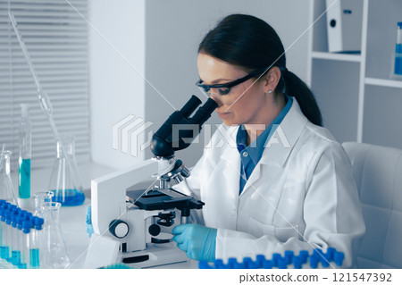 In a modern lab, a skilled female scientist analyzes biological and chemical samples under a microscope, using advanced equipment for precise research vital to health and technology development 121547392