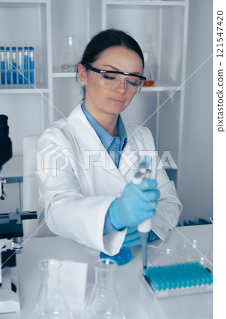 A dedicated female scientist is diligently conducting precise research in a stateoftheart laboratory, utilizing a pipette to handle various liquids with utmost care and attention to detail 121547420