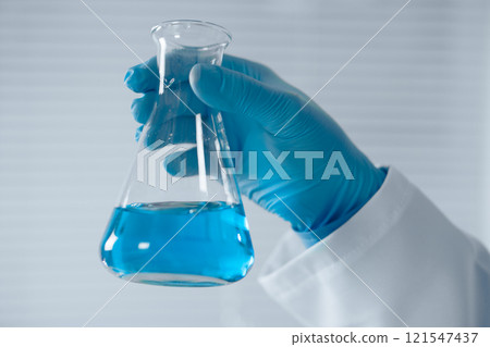 A dedicated scientist holds an Erlenmeyer flask with vibrant blue liquid, conducting experiments in a wellequipped lab, significantly contributing to advancements in science and technology 121547437