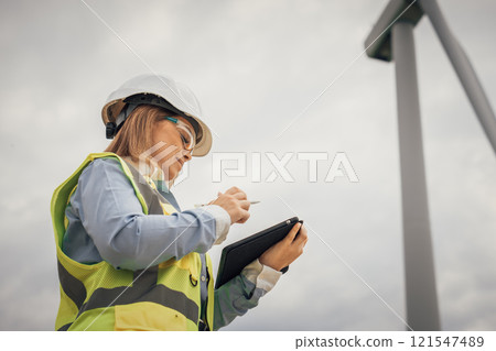 A female engineer is currently inspecting a renewable energy site, using her tablet to monitor various aspects of the project, demonstrating her skills and expertise in technology and sustainability 121547489