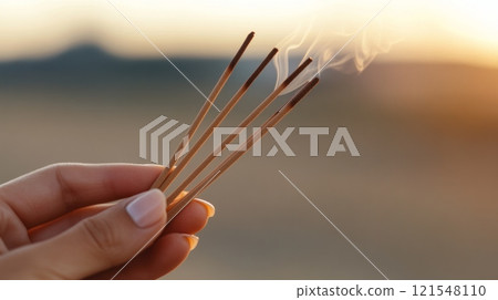 Close up of a hand carefully holding four thin sticks of incense. 121548110