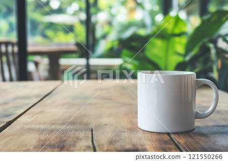 Clean white coffee mug resting on a wooden table in natural light with greenery in the background 121550266