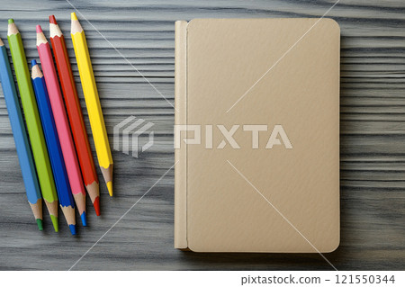 Set of colored pencils and a notebook arranged on a wooden desk with plenty of space for creativity 121550344