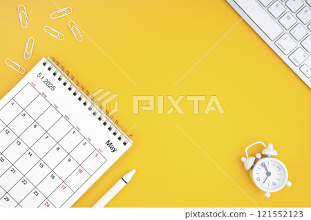 May 2025, Monthly desk calendar for 2025 year and alarm clock with paper clips on yellow color background 121552123