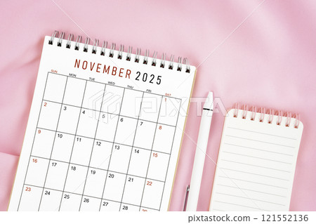 November 2025 month calendar and pen with open diary on pink fabric background. 121552136