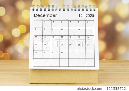 December 2025 desk calendar on wooden table with gold light bokeh. 121552722