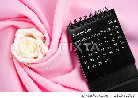 December 2025 desk calendar black color and rose on pink textile. 121552798